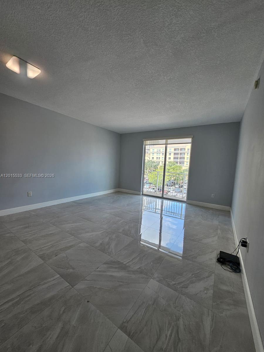 An empty room features gray walls, large light-gray tile flooring, and a sliding glass balcony door — 7270 SW 88th St # B202, Miami FL 33156, MIAMI, FL