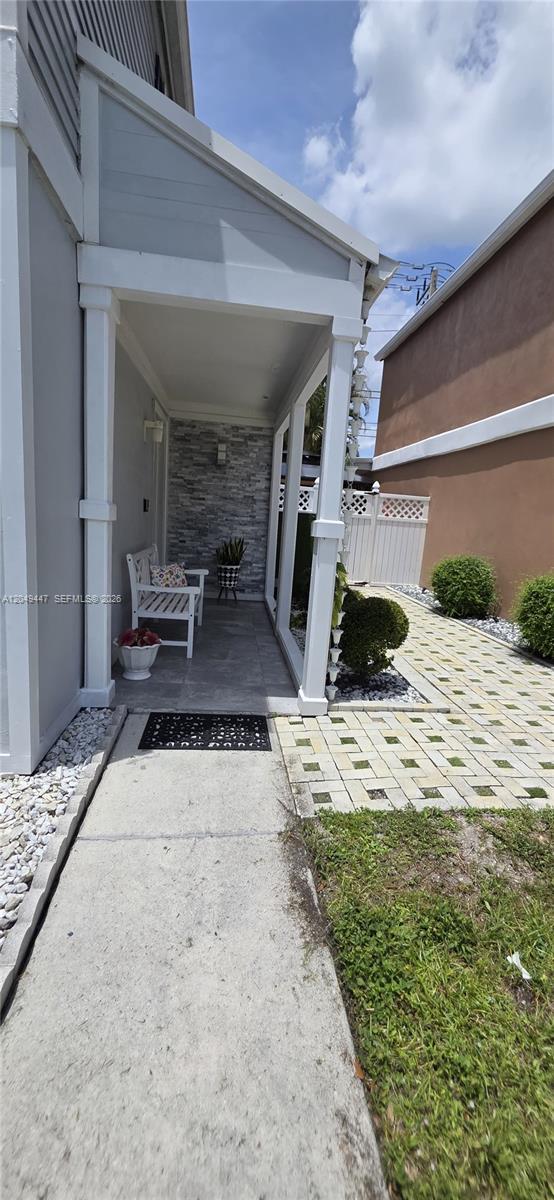 A covered porch with a stone accent wall leads to a paved walkway and yard — 3330 Kapot Ter, Miramar FL 33025, MIRAMAR, FL