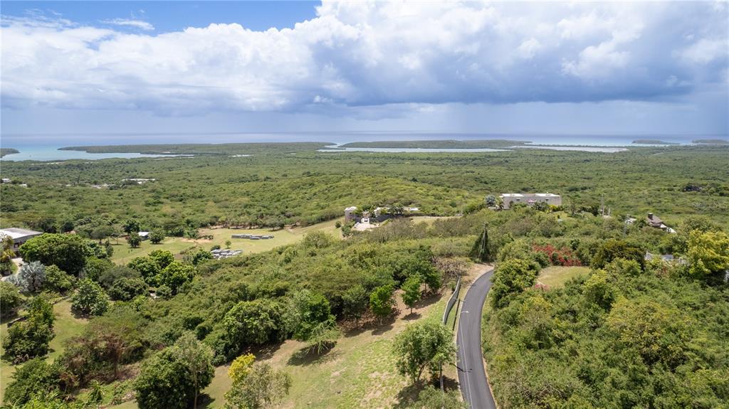 An aerial view shows a winding road leading through a lush, hilly landscape toward the ocean — 18 CALLE 16, VIEQUES, PR