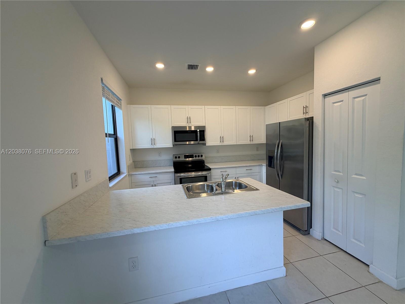 A kitchen features white cabinets, stainless steel appliances, and a marble-patterned countertop island — 13421 SW 287th Ter, Homestead FL 33033, HOMESTEAD, FL