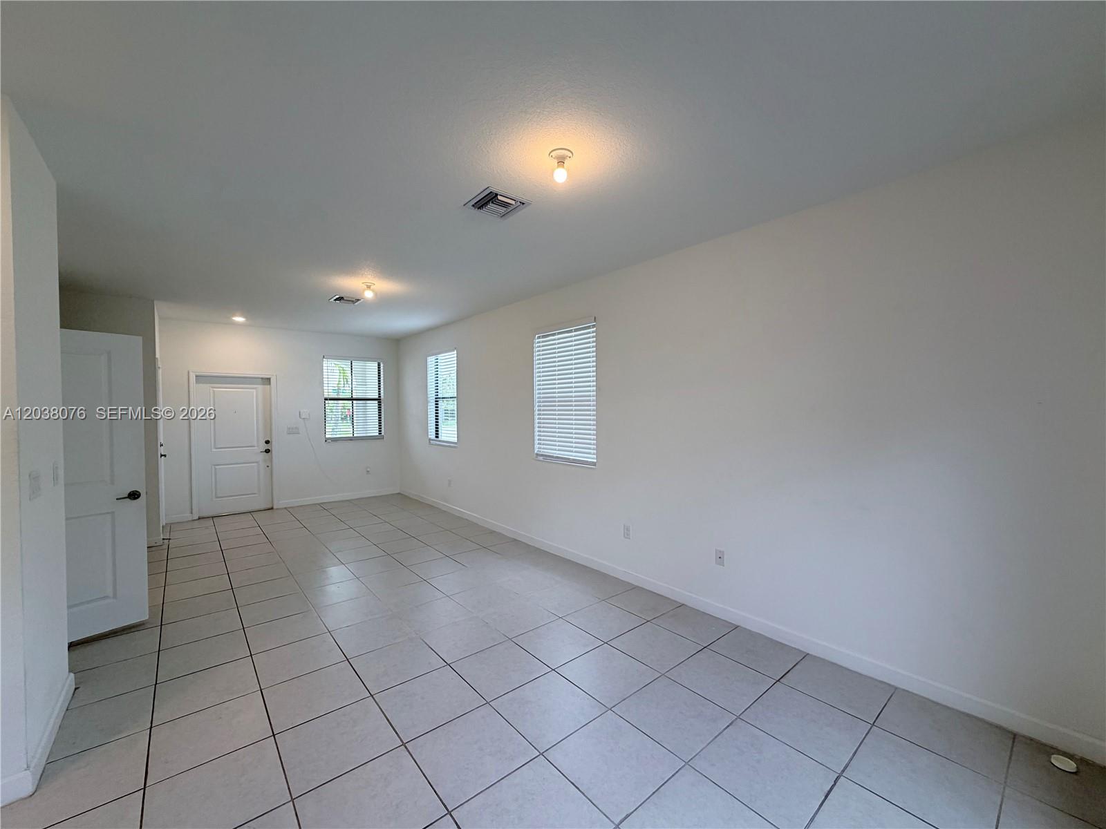 An empty room features white walls, tile flooring, three windows with blinds, and two ceiling lights — 13421 SW 287th Ter, Homestead FL 33033, HOMESTEAD, FL
