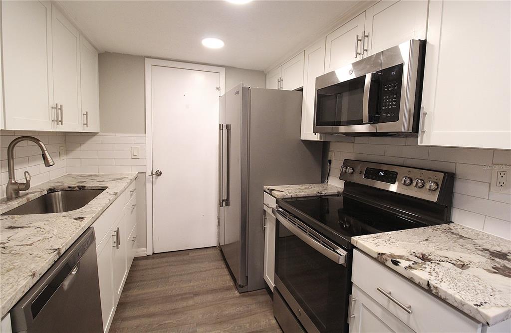 A kitchen features white cabinets, granite countertops, stainless steel appliances, and wood-look flooring — 4119 61ST AVENUE TERRACE W UNIT 407, BRADENTON, FL