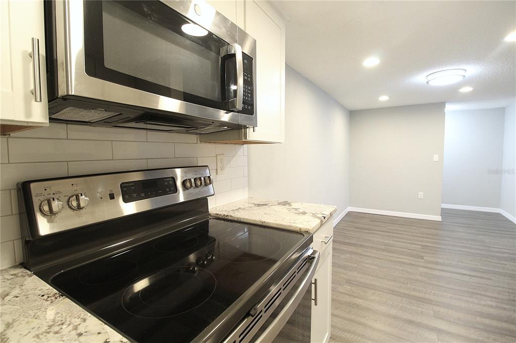 A kitchen with stainless steel appliances, white cabinets, and granite countertops overlooks an adjacent room — 4119 61ST AVENUE TERRACE W UNIT 407, BRADENTON, FL