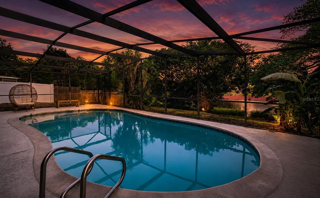 A swimming pool with a screened enclosure overlooks a lake at sunset — 146 LAKE RING DRIVE, WINTER HAVEN, FL