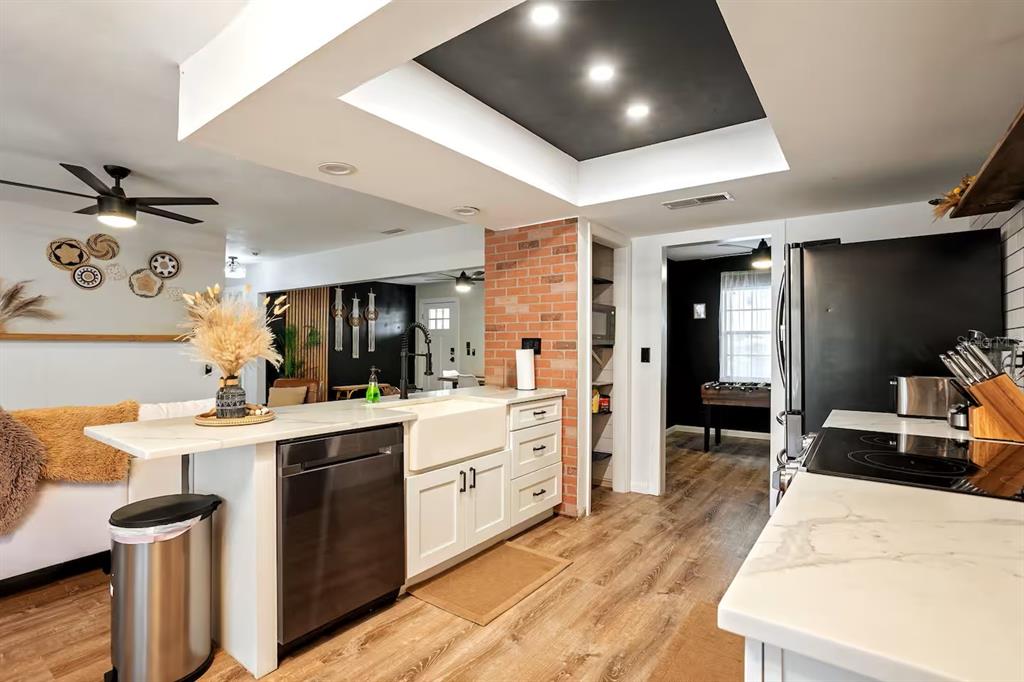 A kitchen features white cabinets, a farmhouse sink, a brick accent wall, and a tray ceiling — 146 LAKE RING DRIVE, WINTER HAVEN, FL