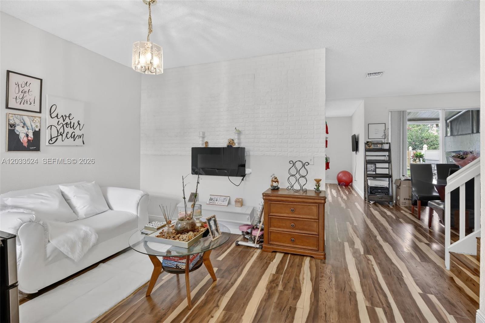 A living room features white walls, a brick accent wall, and wood-patterned flooring — PEMBROKE PINES, FL