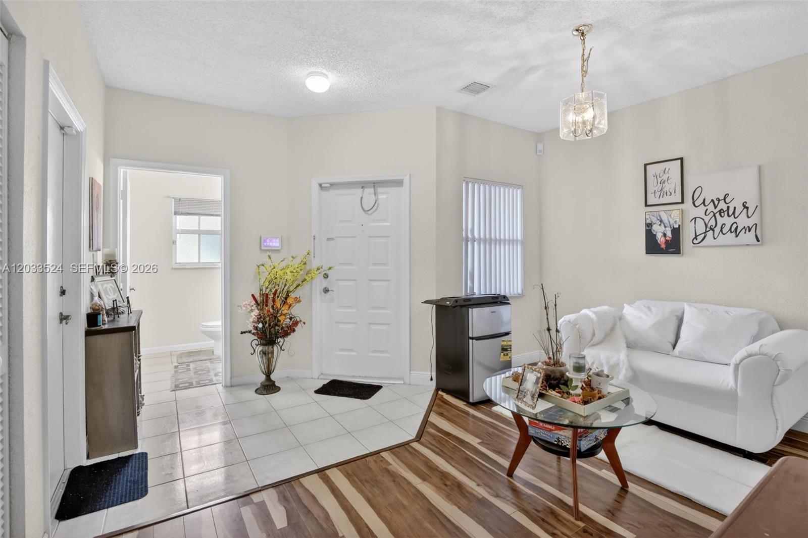 An entryway with tile flooring transitions into a living area with wood-look floors and furniture — PEMBROKE PINES, FL