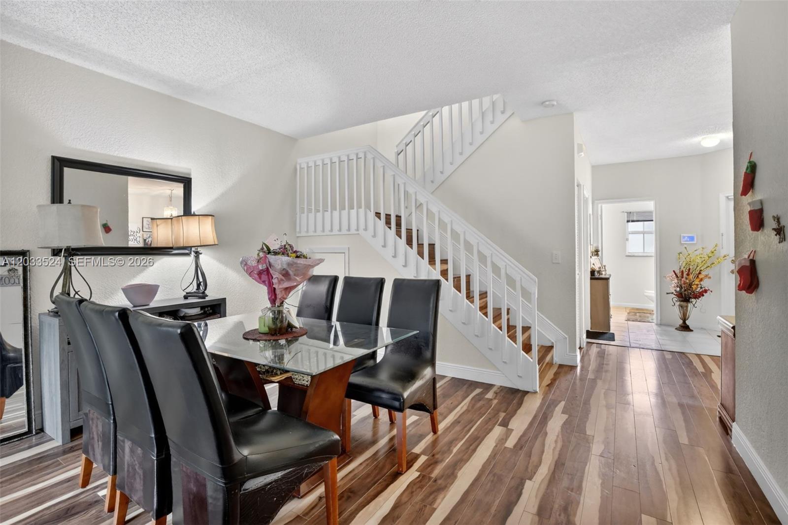 A dining area features a glass table, black chairs, and a staircase with white railings — PEMBROKE PINES, FL