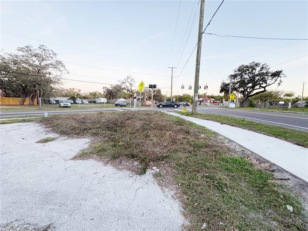 A vacant, overgrown corner lot sits at a paved intersection with a sidewalk and traffic lights — 535 MAYDELL DRIVE, TAMPA, FL