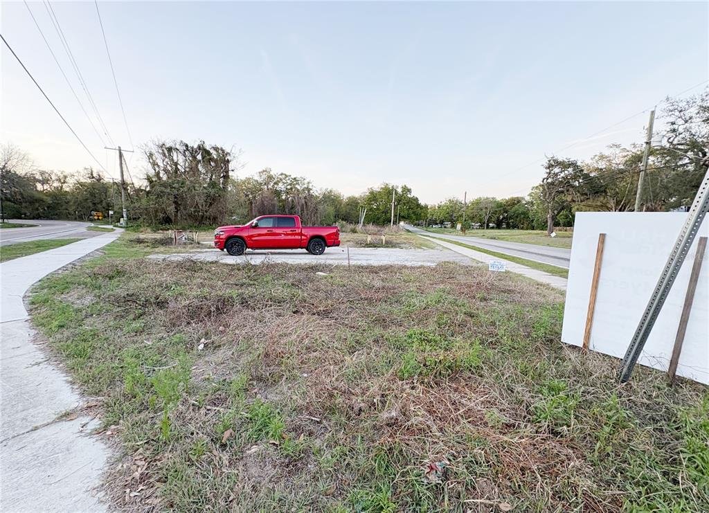 A red pickup truck is parked on a vacant, grassy lot next to a sidewalk — 535 MAYDELL DRIVE, TAMPA, FL