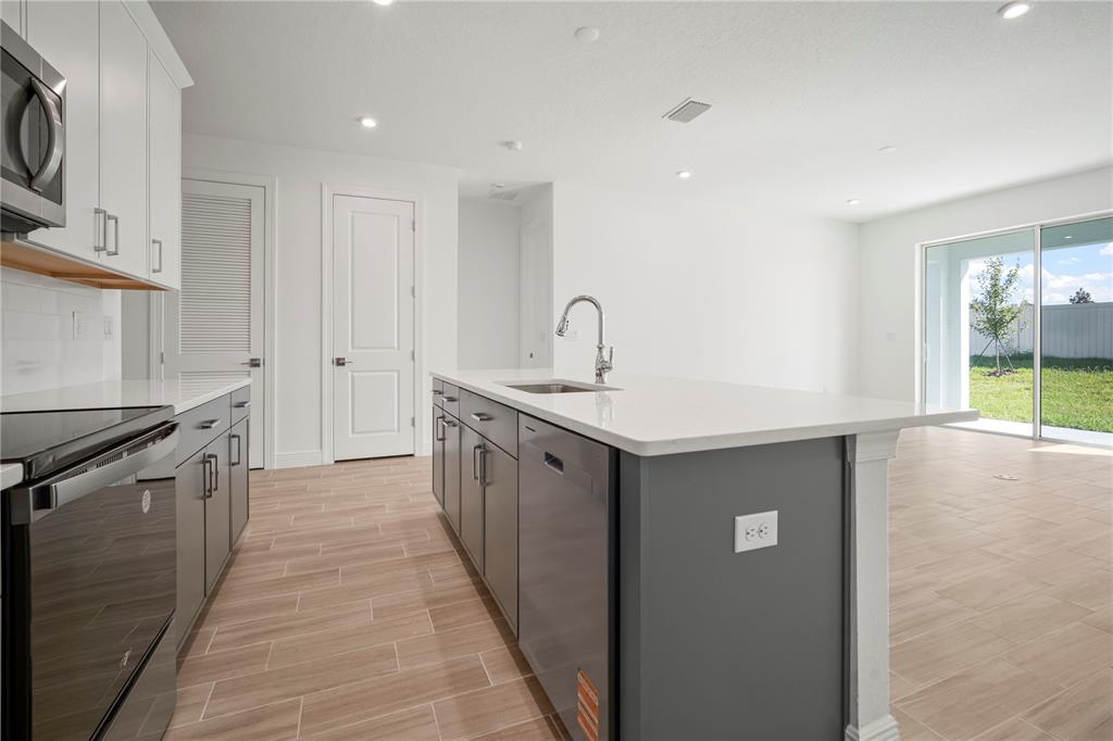 A modern kitchen features gray cabinets, white countertops, stainless steel appliances, and tile flooring — 2949 STEWART CREEK CIRCLE, PLANT CITY, FL