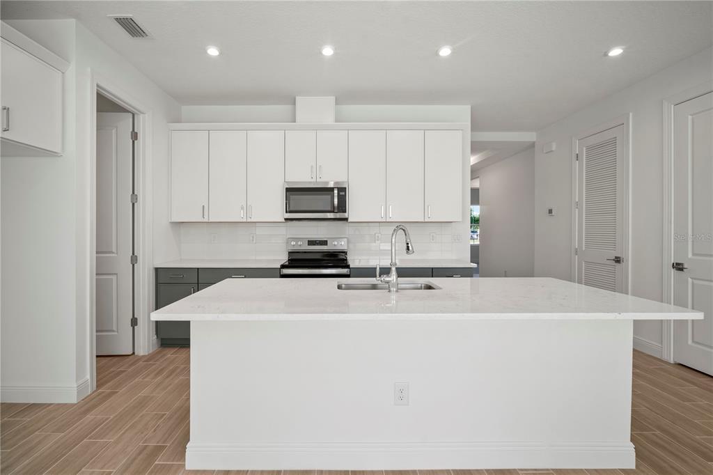 A modern kitchen features white upper cabinets, dark lower cabinets, and a large quartz island — 2949 STEWART CREEK CIRCLE, PLANT CITY, FL