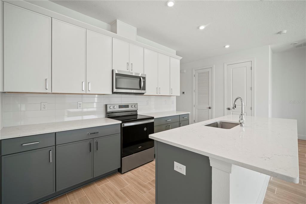 A modern kitchen features white upper cabinets, gray lower cabinets, and a white quartz island — 2949 STEWART CREEK CIRCLE, PLANT CITY, FL