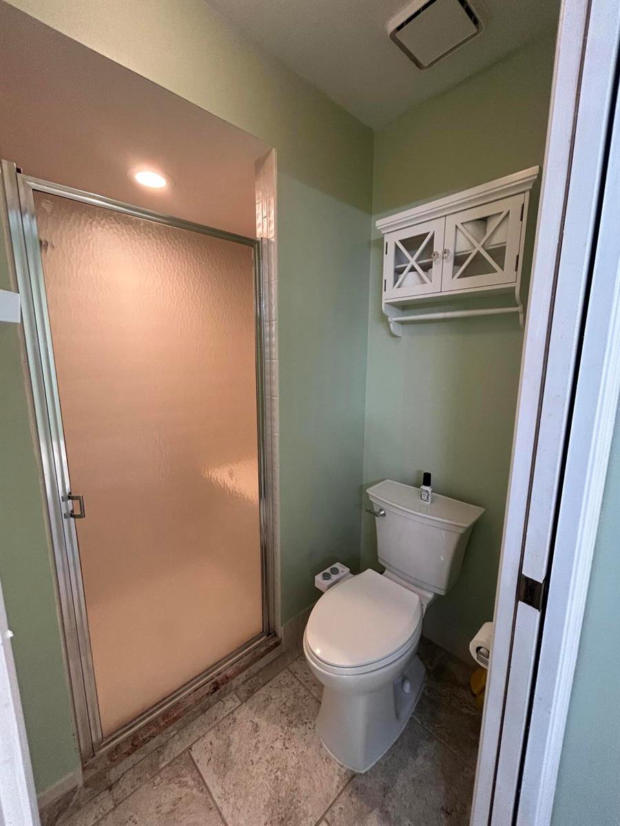 A bathroom with a glass-enclosed shower, a white toilet, and a wall-mounted cabinet — 6376 Breckenridge Circle, Lake Worth FL 33467, LAKE WORTH, FL