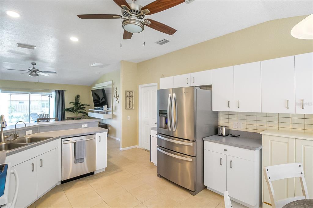A kitchen with white cabinets, stainless steel appliances, and tile flooring opens to a living area — 1465 SHIELDS STREET, PUNTA GORDA, FL