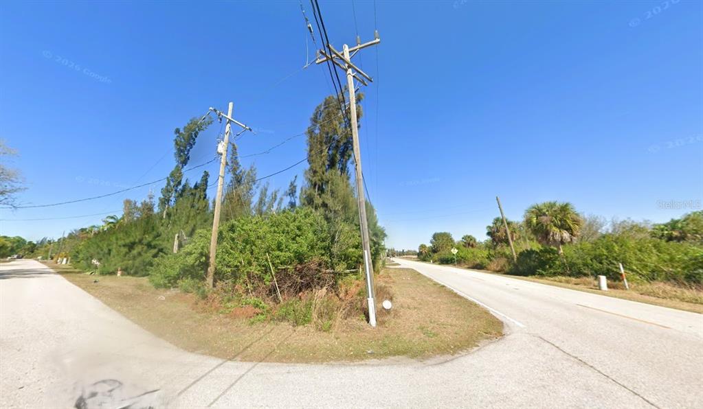 A paved road curves past a grassy lot with utility poles and dense vegetation — 101 GLENHOLM AVENUE, PUNTA GORDA, FL