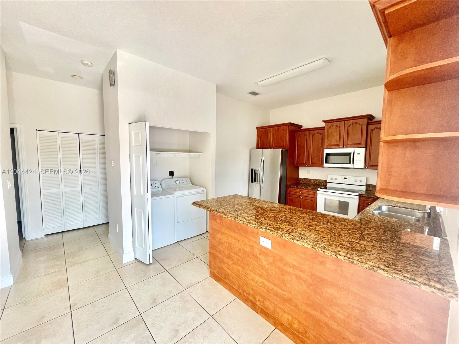 A kitchen features wood cabinets, granite countertops, and an adjacent laundry closet with appliances — 2487 W 5th Ct, Hialeah FL 33010, HIALEAH, FL