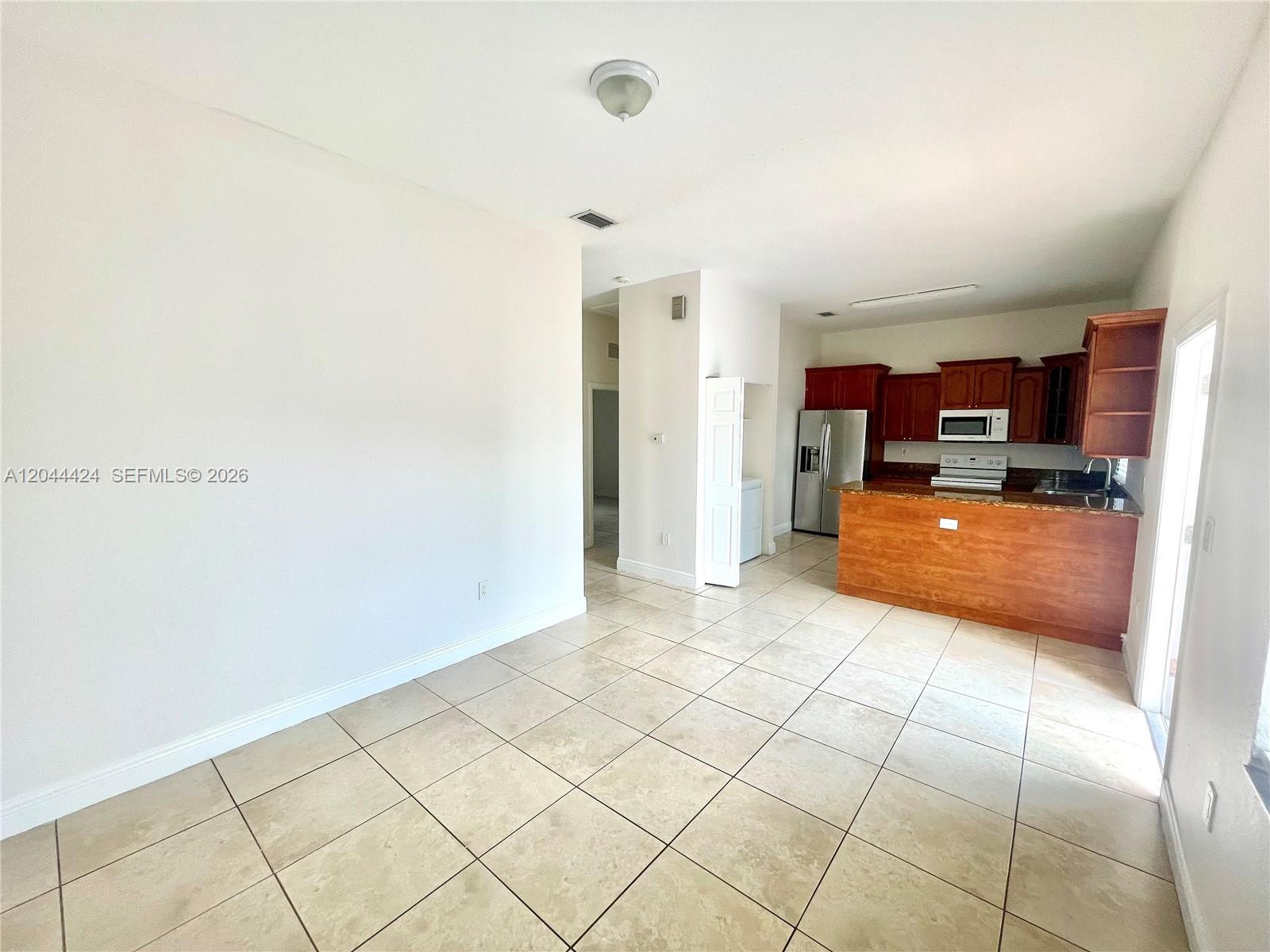 An open-concept kitchen with wood cabinets and tile flooring connects to a living area — 2487 W 5th Ct, Hialeah FL 33010, HIALEAH, FL