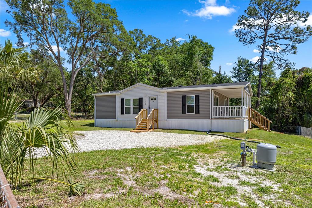 A single-story manufactured home with grey siding, a front porch, and a gravel driveway — 17360 SE 65TH STREET, OCKLAWAHA, FL