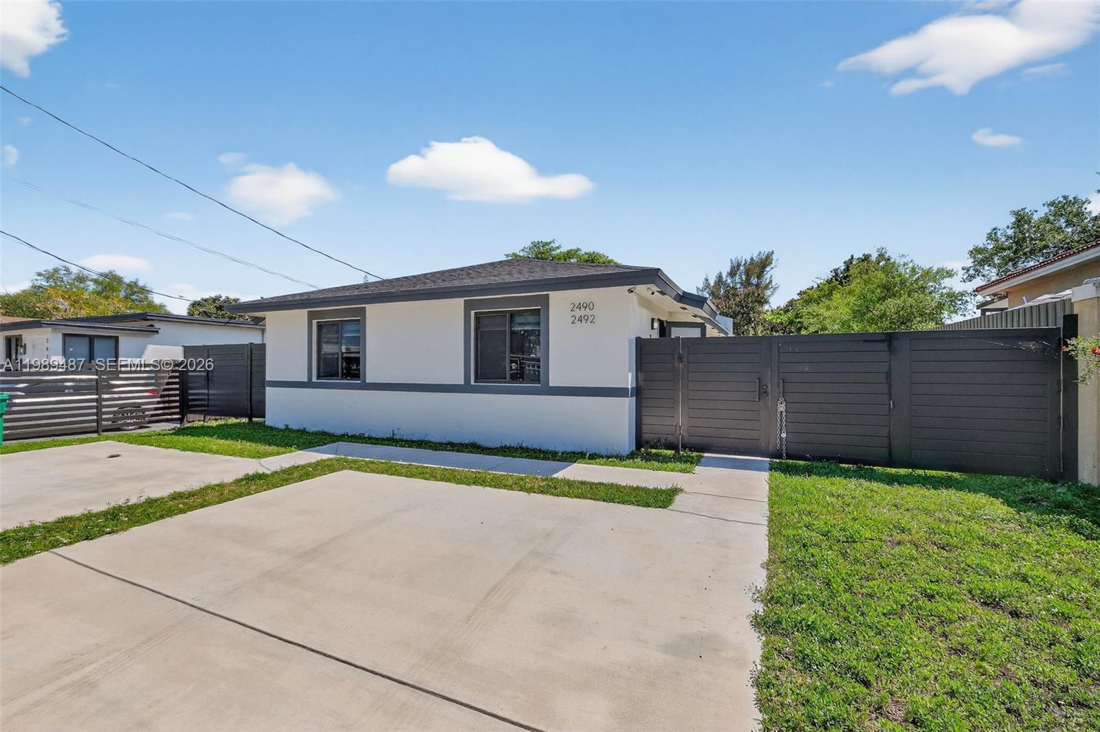 A single-story white house with dark trim features a concrete driveway and a wooden fence — 2490 NW 44th St # 2490, Miami FL 33142, MIAMI, FL