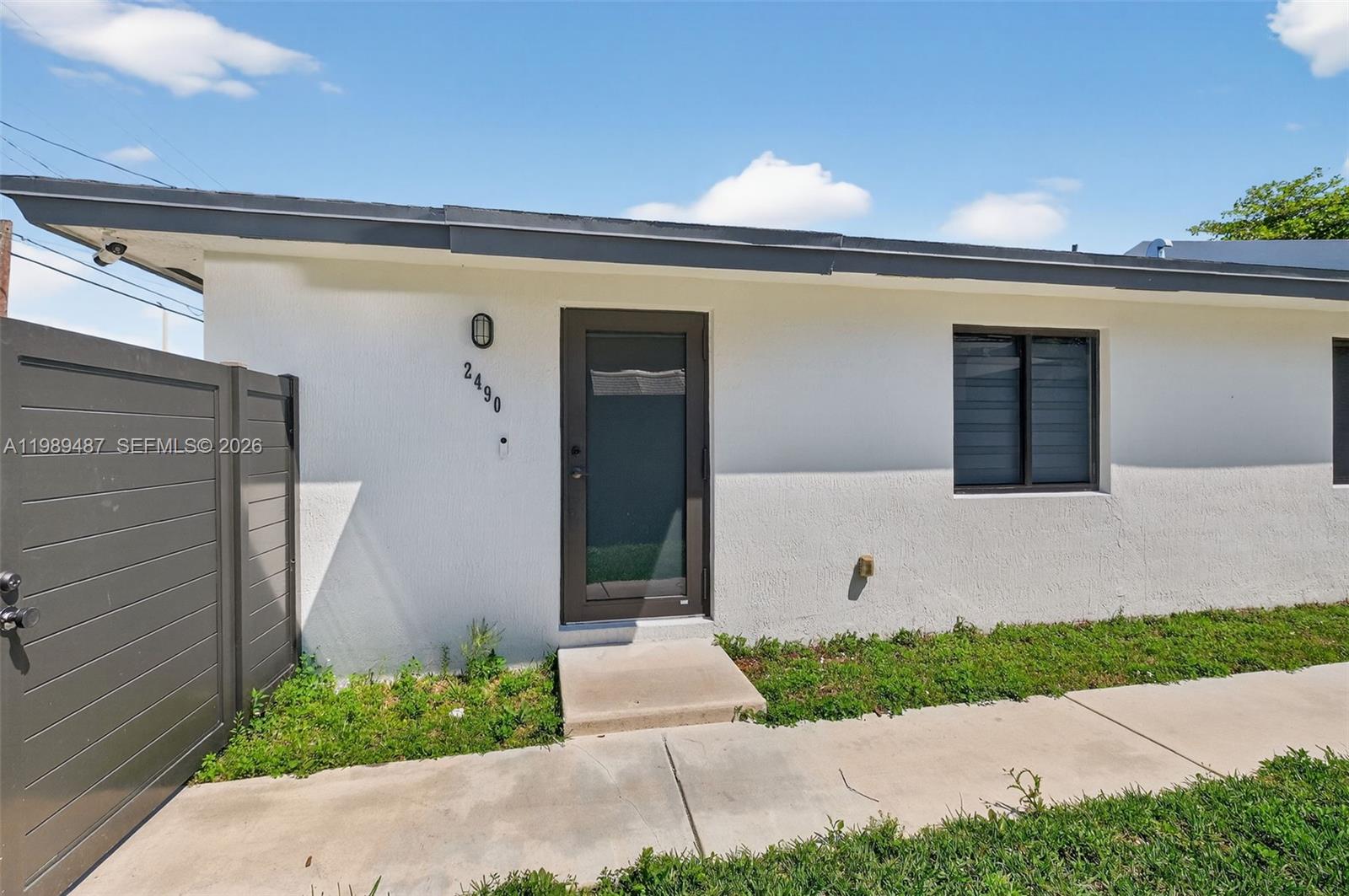 The exterior of a white house features a dark-framed door, a window, and a fence — 2490 NW 44th St # 2490, Miami FL 33142, MIAMI, FL