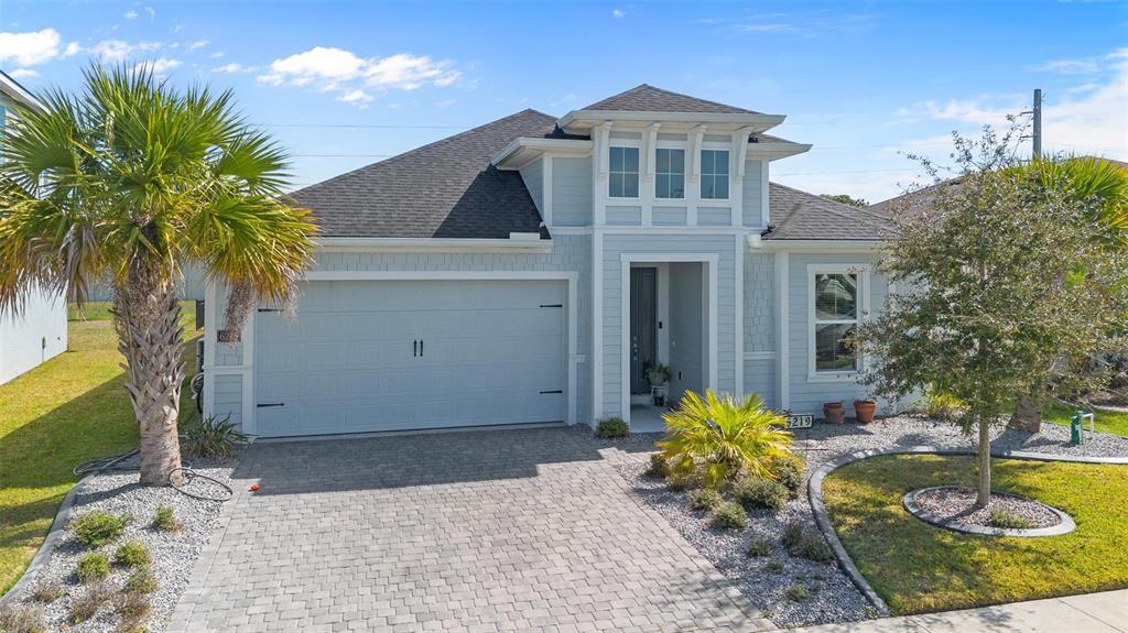 A light blue single-story house features a two-car garage, a paved driveway, and palm trees — 6219 WOODHAVEN VILLAGE DRIVE, PORT ORANGE, FL