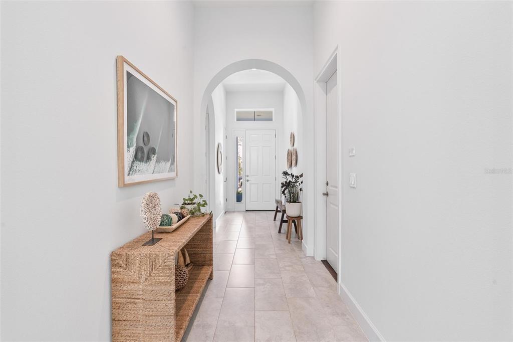 A bright entryway features a woven console table, arched doorway, and light-colored tile flooring — 6219 WOODHAVEN VILLAGE DRIVE, PORT ORANGE, FL