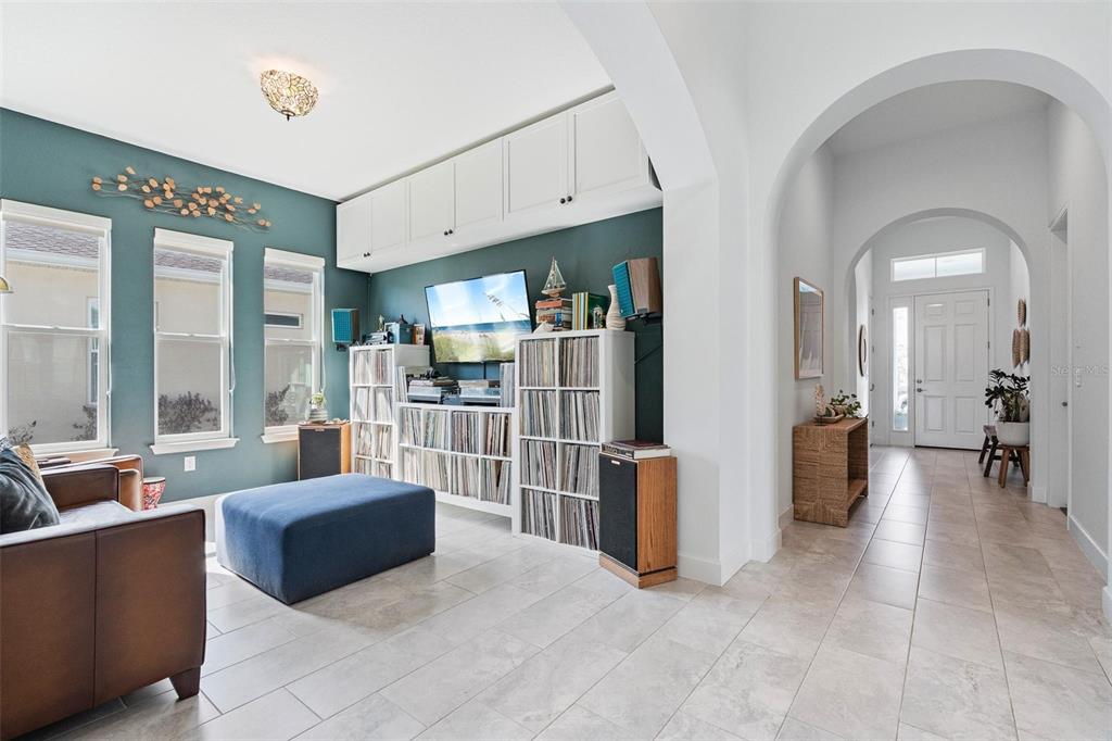 A living room features teal walls, white storage cabinets, vinyl record shelving, and tiled floors — 6219 WOODHAVEN VILLAGE DRIVE, PORT ORANGE, FL