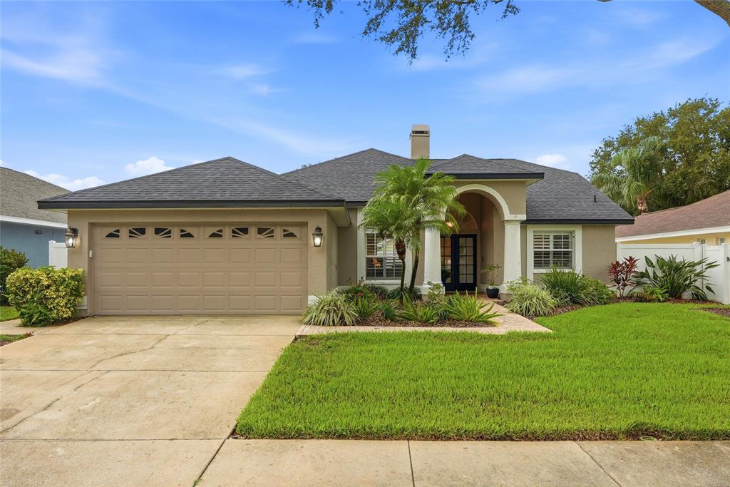 A single-story house with a tan stucco exterior, a two-car garage, and a front entryway — 1258 PARADISE LAKE DRIVE, TARPON SPRINGS, FL