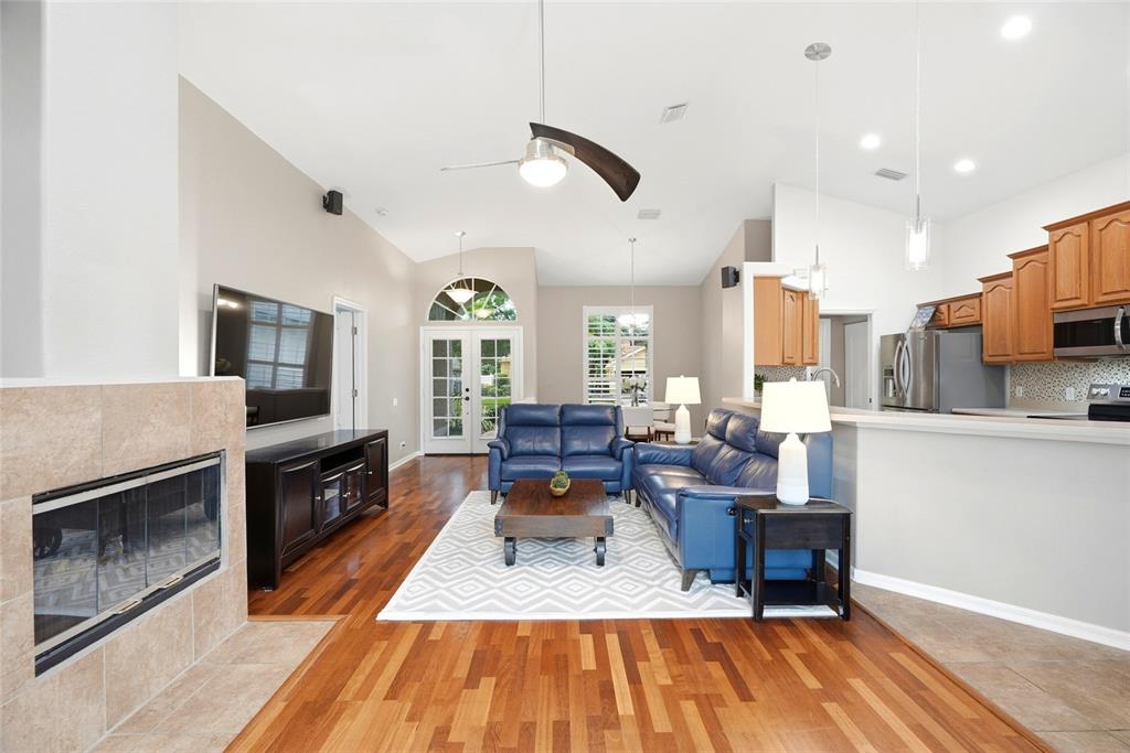 A living room with hardwood floors, a fireplace, blue leather furniture, and an open kitchen — 1258 PARADISE LAKE DRIVE, TARPON SPRINGS, FL