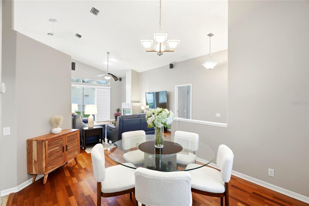 A dining area with a glass table and chairs sits before a living room space — 1258 PARADISE LAKE DRIVE, TARPON SPRINGS, FL