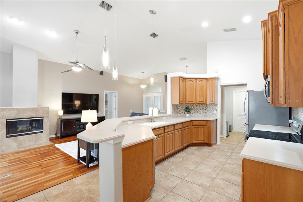 A kitchen with oak cabinets and a breakfast bar overlooks a living room with fireplace — 1258 PARADISE LAKE DRIVE, TARPON SPRINGS, FL