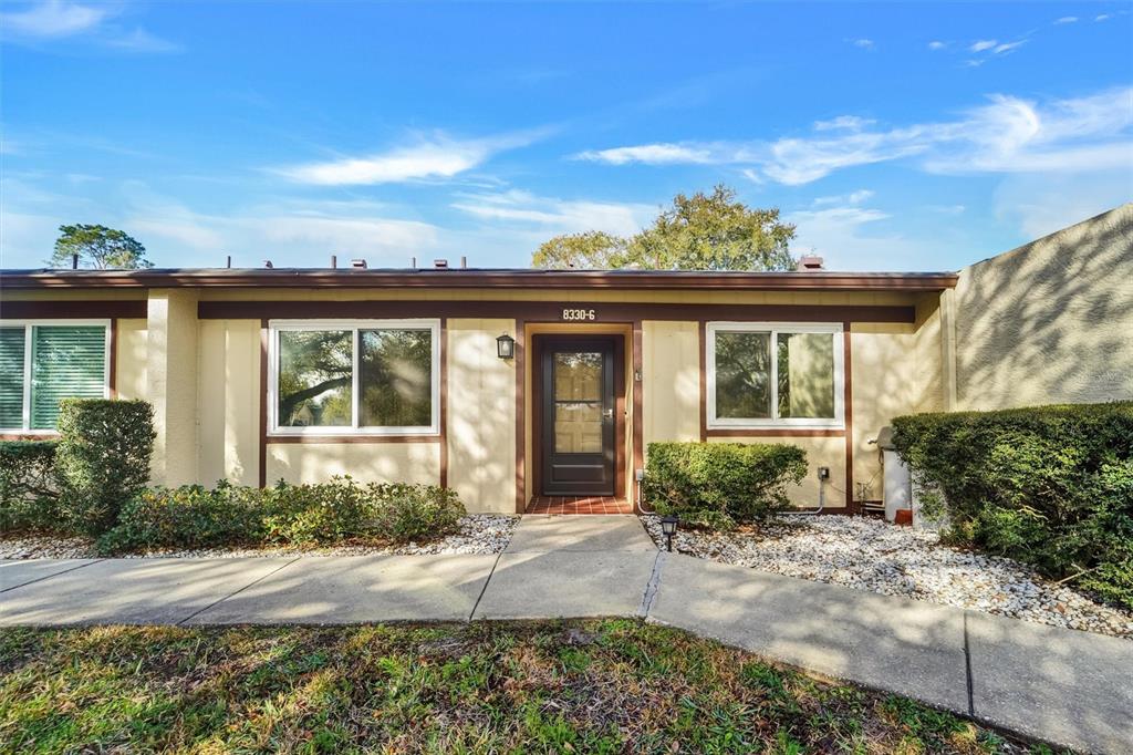 A single-story residential building exterior features a central front door, two windows, and landscaping — 8330 HIGH POINT CIRCLE UNIT 6, PORT RICHEY, FL