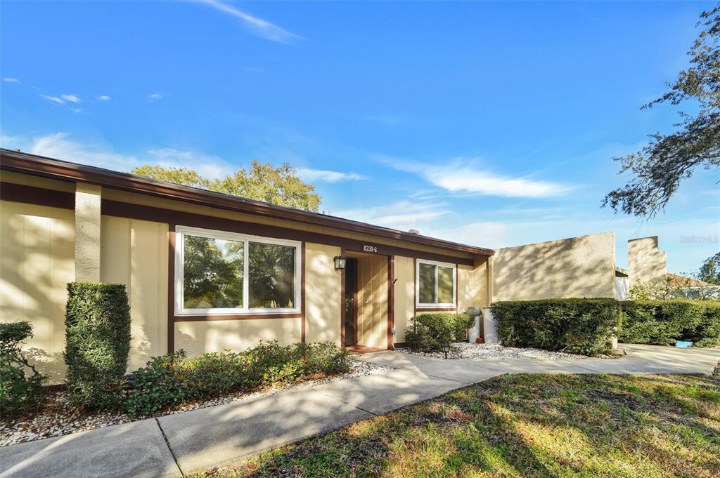 A single-story house exterior features a concrete walkway, tan siding, brown trim, and landscaping — 8330 HIGH POINT CIRCLE UNIT 6, PORT RICHEY, FL