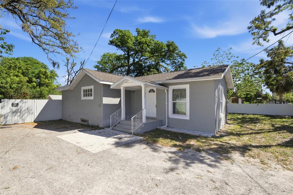 A gray, single-story house with a white front door and a gravel driveway — 1410 E WATERS AVENUE, TAMPA, FL
