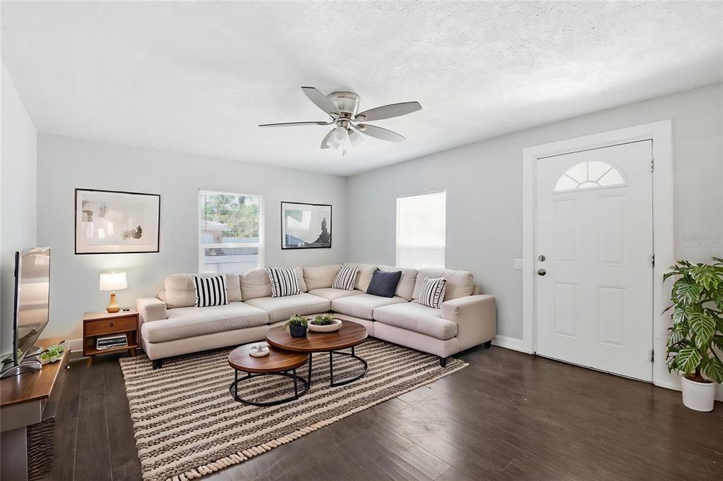 A living room features a sectional sofa, two round coffee tables, and dark wood flooring — 1410 E WATERS AVENUE, TAMPA, FL