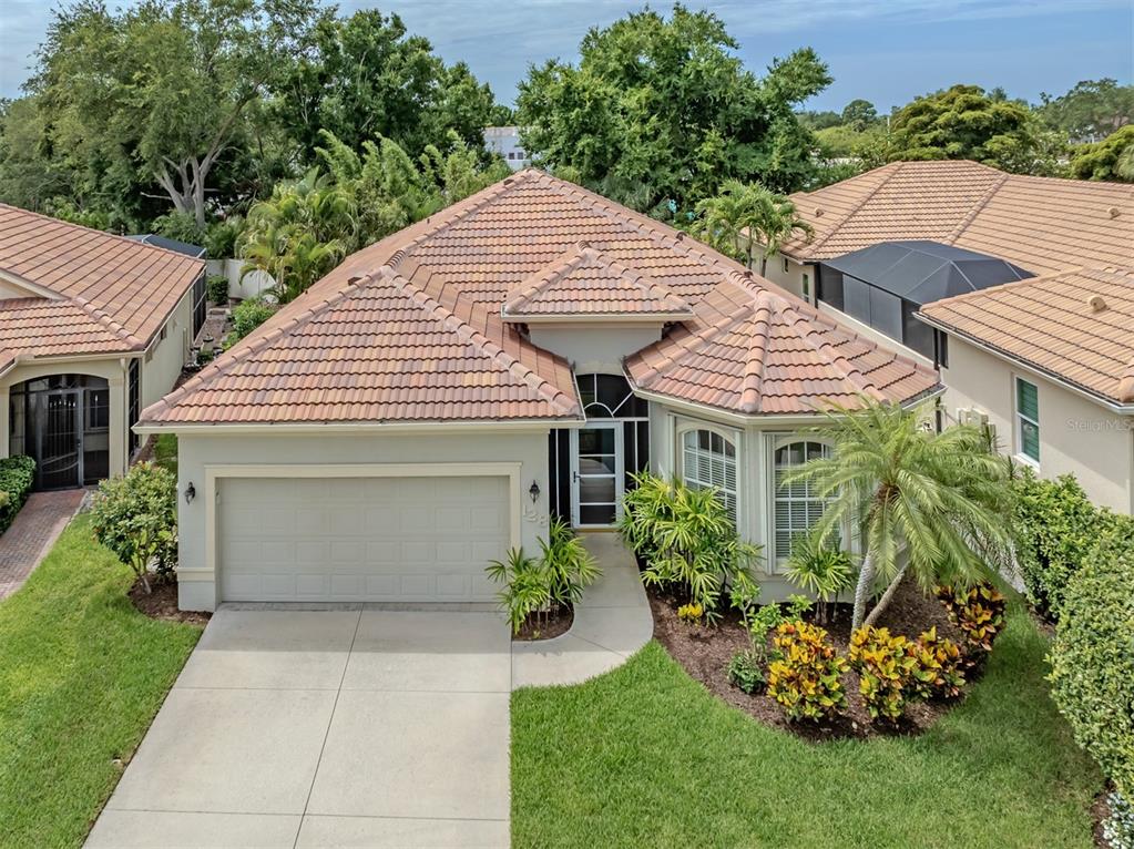 An aerial view of a single-story house with a tiled roof, garage, and landscaped yard — 128 AMORA AVENUE, VENICE, FL