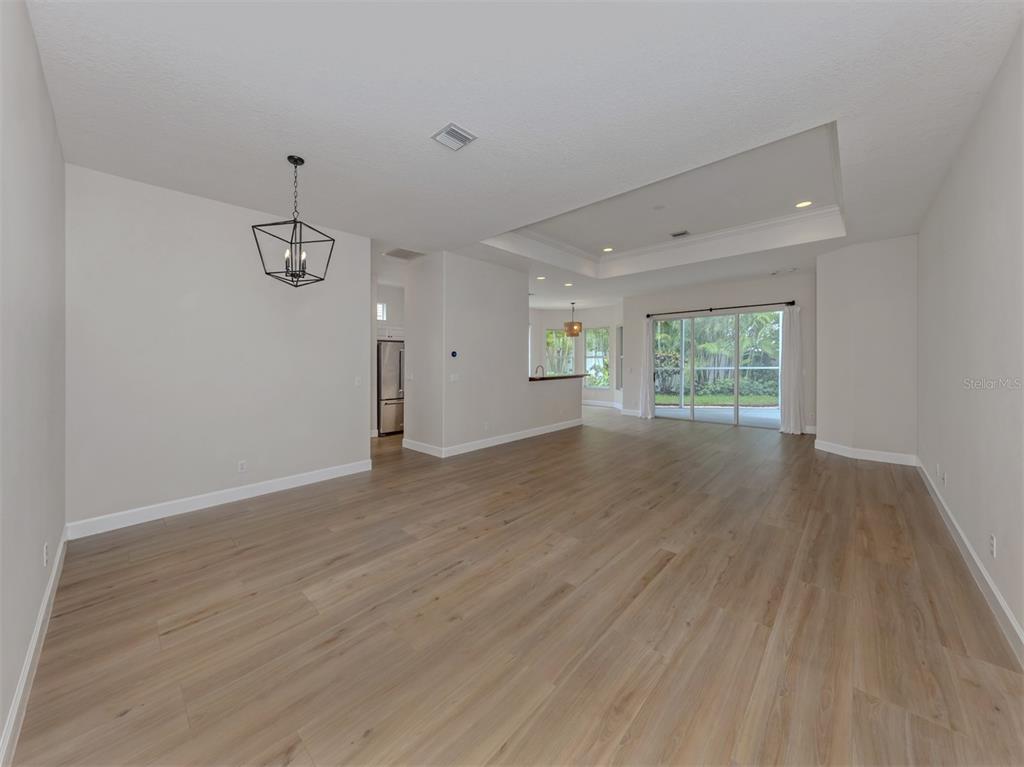 An open-concept living and dining area features light wood-look flooring and a tray ceiling — 128 AMORA AVENUE, VENICE, FL