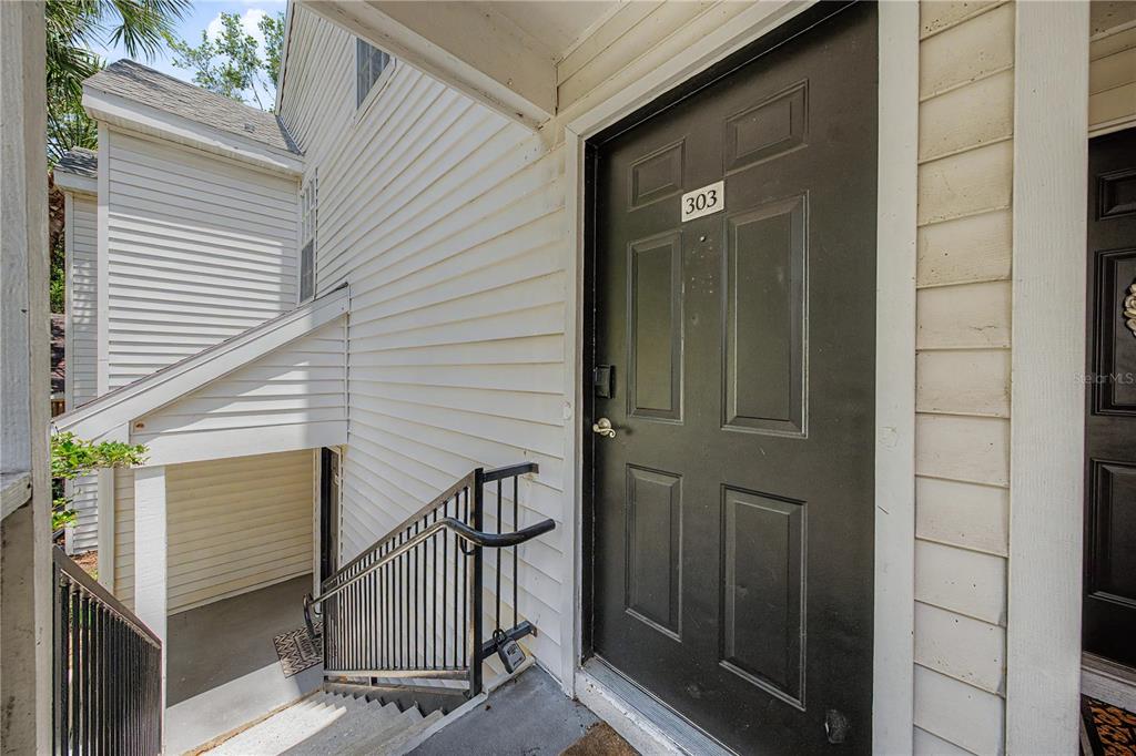 A black front door labeled 303 is at the top of an outdoor concrete staircase — 3266 HAVILAND COURT UNIT 303, PALM HARBOR, FL