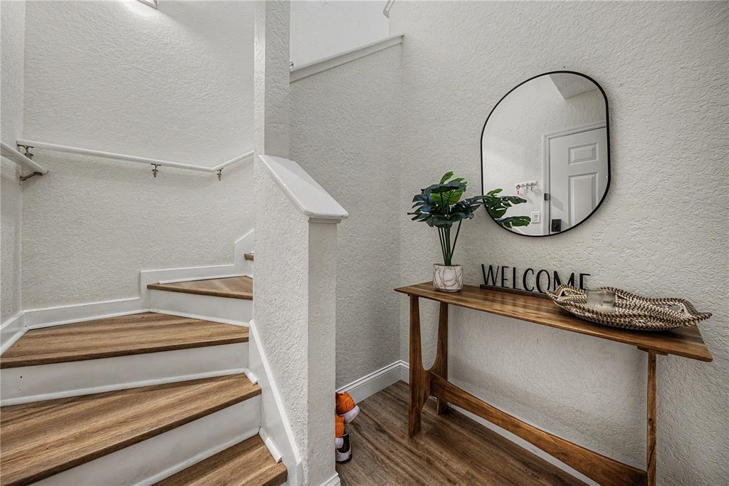 A staircase with wood-look treads sits beside a wooden console table and a wall mirror — 3266 HAVILAND COURT UNIT 303, PALM HARBOR, FL