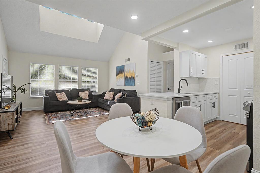 An open-concept living and dining area features light wood flooring, white cabinetry, and a skylight — 3266 HAVILAND COURT UNIT 303, PALM HARBOR, FL