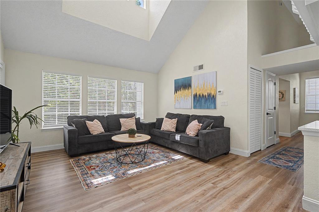 A living room features a vaulted ceiling, gray sofas, a round coffee table, and wood-look flooring — 3266 HAVILAND COURT UNIT 303, PALM HARBOR, FL