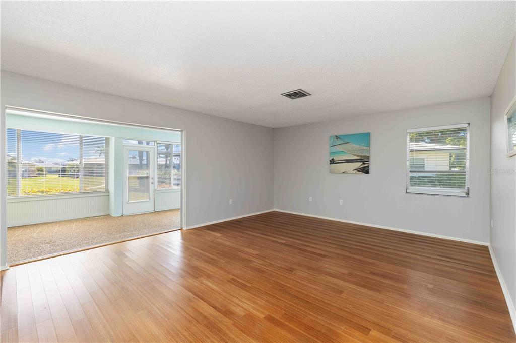 An empty living room with wood-look flooring, light gray walls, and a sliding door to a lanai — 7011 9TH AVENUE W, BRADENTON, FL