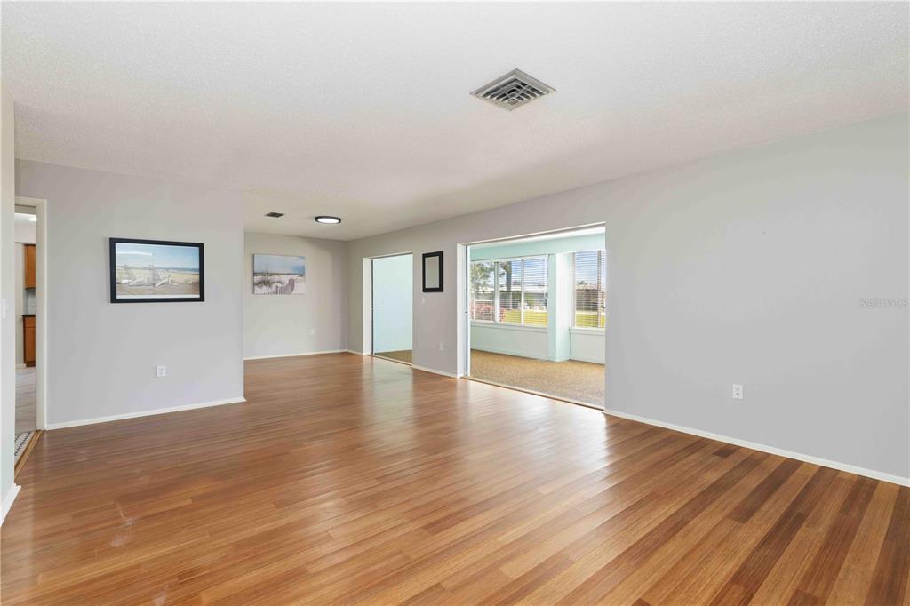 A spacious living room features light gray walls, wood-look flooring, and a sliding glass door — 7011 9TH AVENUE W, BRADENTON, FL