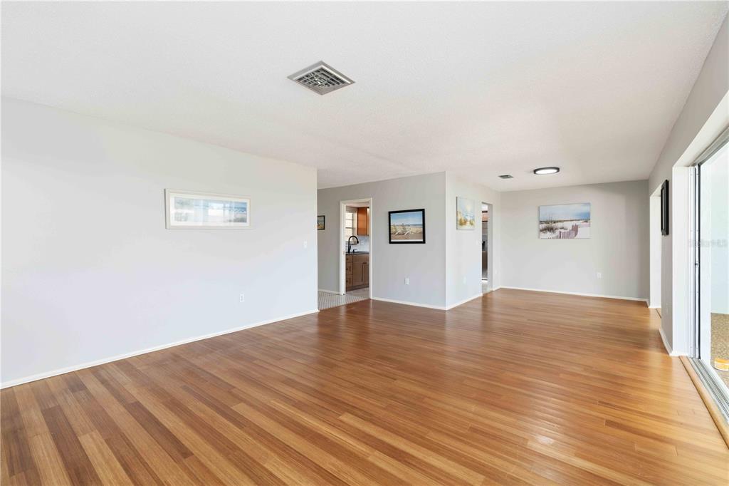 An empty living room features light gray walls, wood flooring, and a sliding glass door — 7011 9TH AVENUE W, BRADENTON, FL