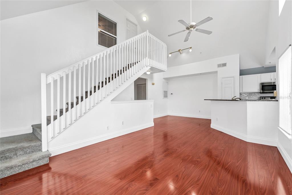 A bright living area features hardwood floors, a white staircase, and an open kitchen — 9013 LEE VISTA BOULEVARD UNIT 1910, ORLANDO, FL
