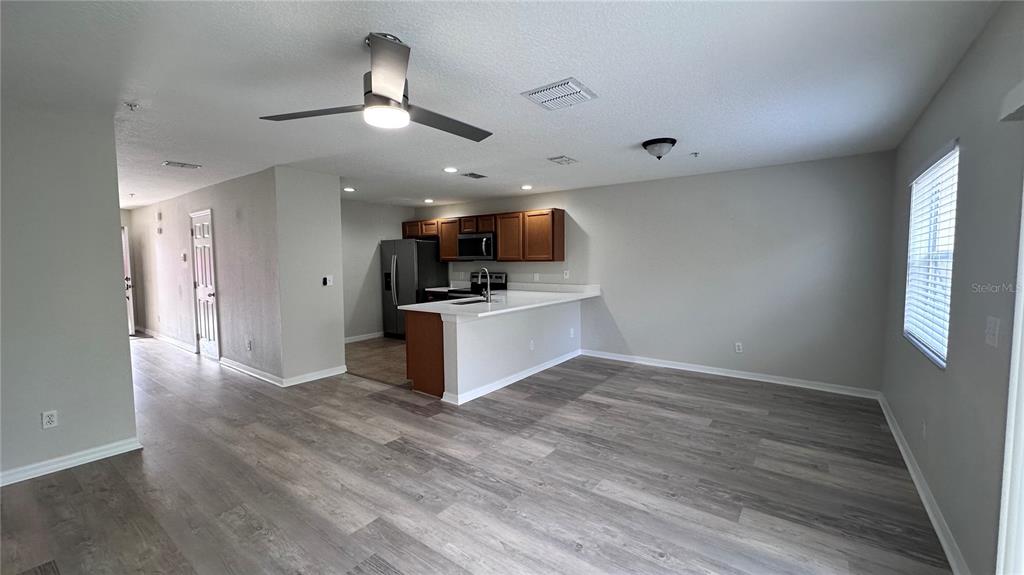 An open-concept kitchen with wood cabinets and a breakfast bar overlooks a living area — 517 INTERLUDE LANE UNIT H-105, ORLANDO, FL