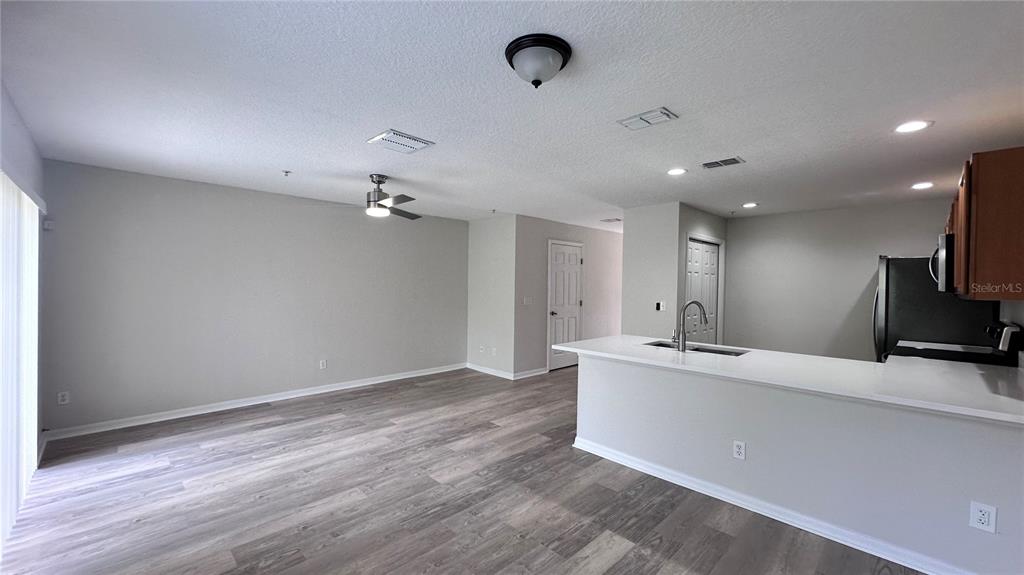 An open-concept living area features wood-look flooring, a ceiling fan, and a kitchen island — 517 INTERLUDE LANE UNIT H-105, ORLANDO, FL