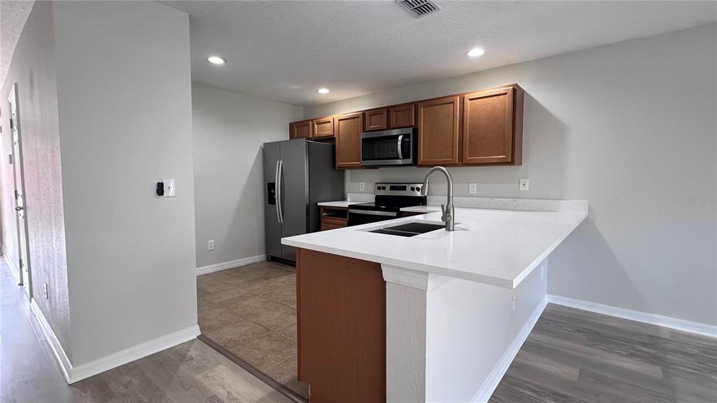 A kitchen features wood cabinets, stainless steel appliances, and a white quartz breakfast bar — 517 INTERLUDE LANE UNIT H-105, ORLANDO, FL