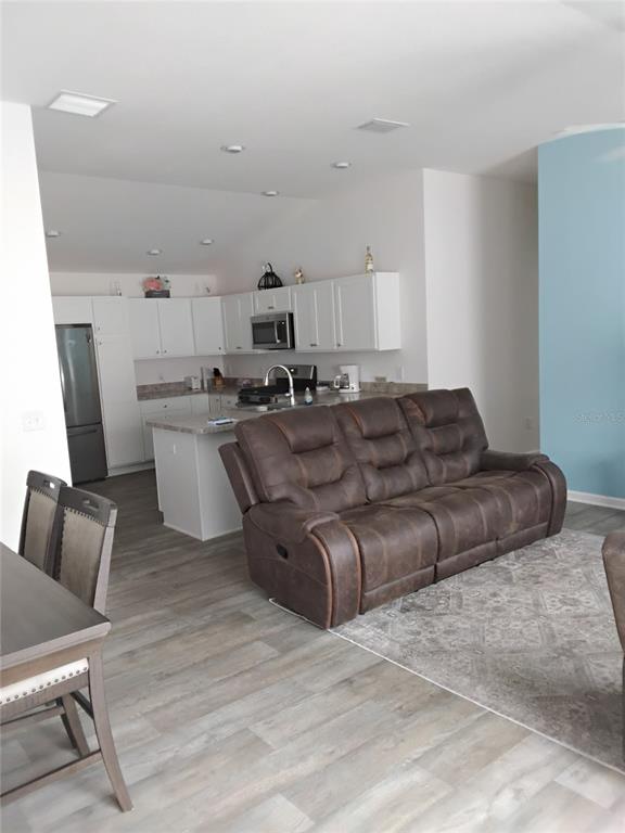 A kitchen with white cabinets and a brown reclining sofa in an open-concept living area — 3561 COCHRAN STREET, THE VILLAGES, FL
